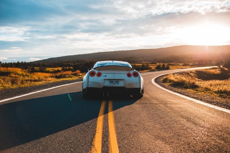 A sportscar driving along a deserted road into the sunset